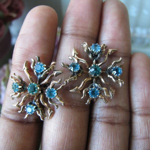 May include: A pair of gold tone earrings with a floral design and blue and green rhinestones.