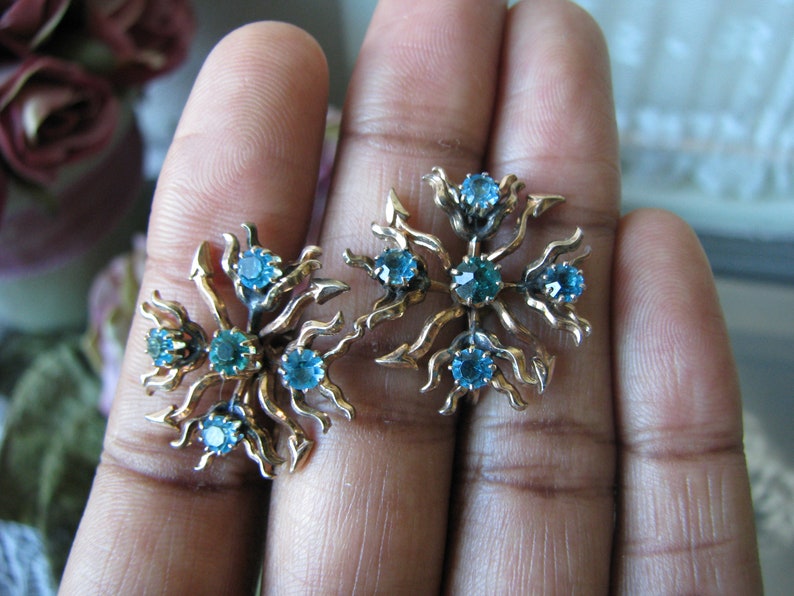 May include: A pair of gold tone earrings with a floral design and blue and green rhinestones.