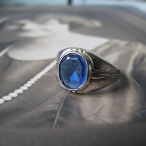 Op de afbeelding: Een zilveren ring met een grote, ovale blauwe edelsteen in het midden. De ring heeft een eenvoudig, klassiek ontwerp.