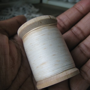 Op de afbeelding: Een houten spoel met witte draad.
