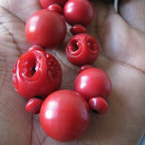 Peut inclure: Un collier de perles rouges avec des d&eacute;tails sculpt&eacute;s. Les perles sont rondes et lisses, et le collier est enfil&eacute; sur un cordon.