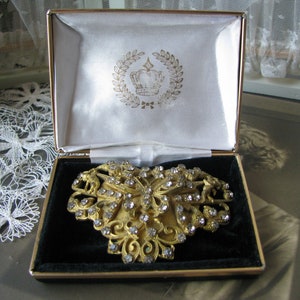 May include: A gold-tone brooch in the shape of a butterfly with clear rhinestones. The brooch is in a black velvet-lined box with a white satin interior. The box has a gold crown logo with a laurel wreath.