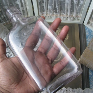 May include: A clear glass bottle with a rounded top and a slightly frosted finish. The bottle is empty and appears to be vintage.