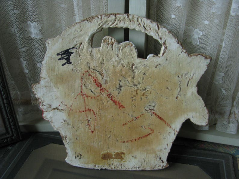 May include: A white wooden plaque with a cutout design and red markings. The plaque has a rough, textured surface and appears to be vintage.