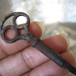 May include: A rusty metal key with a unique, three-hole design in the head. The key is held in a hand.