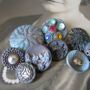 May include: A collection of vintage buttons with various designs and colors, including blue, green, brown, and silver. Some buttons have intricate patterns, while others feature colorful rhinestones.