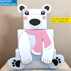 May include: A DIY polar bear gift tower constructed from white boxes, adorned with a pink polka-dot scarf and bear face details. The design includes large paws with black paw prints and the text "Instant Download". The text "Polar Bear Girl Gift Tower DIY" is also visible.