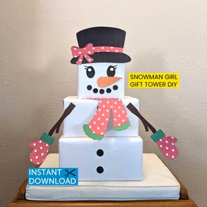May include: A DIY snowman gift tower made from white boxes, featuring a black top hat with a pink bow, a carrot nose, and a pink polka-dot scarf and mittens. The text "Snowman Girl Gift Tower DIY" is visible.
