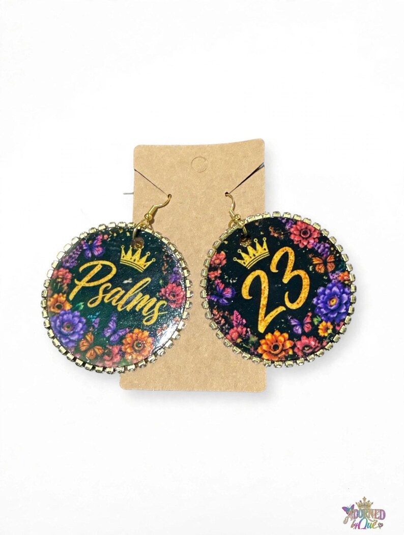 May include: A pair of round dangle earrings featuring a black background with colourful floral patterns and butterflies. The left earring displays the gold text Psalms and a crown, while the right earring shows the number 23 and a crown.