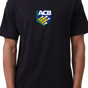 May include: A black short-sleeved t-shirt featuring a centred shield-shaped logo on the chest. The logo displays the letters ACB in white above a blue background with yellow diagonal stripes and white stars, bordered by a green angled edge.