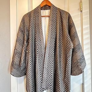 May include: A haori jacket featuring a repeating black, gray, and white checkered pattern throughout the fabric. The garment has wide sleeves, an open front design, and a solid white lining visible along the inner collar and front edges.