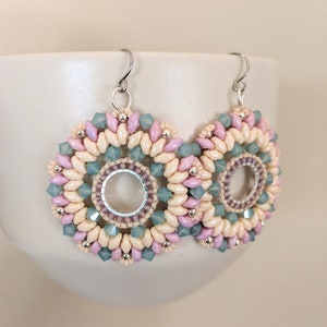 May include: A pair of dangle earrings with a circular design featuring cream, pink, and light blue beads. The earrings have silver hooks.