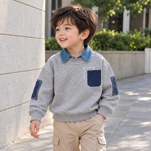 Può includere: Una felpa grigia a maniche lunghe con colletto in denim blu, una tasca sul petto blu scuro con dettagli di cuciture bianche e toppe rettangolari blu scuro su ogni gomito con cuciture a croce bianche, abbinata a pantaloni cargo color sabbia.