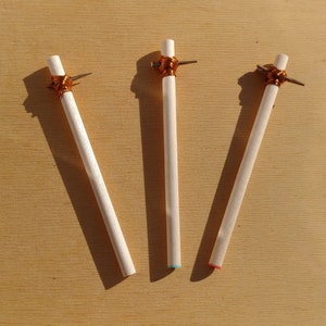 Può includere: Tre pioli di legno con filo di rame avvolto attorno alla parte superiore. I pioli sono su una superficie di legno marrone chiaro. I pioli hanno lunghezze diverse e punte di colori diversi.