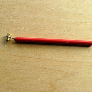 Puede incluir: Una herramienta roja y de latón con una punta puntiaguda, utilizada para punteado o la creación de pequeños detalles en manualidades.