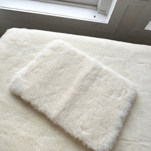 May include: A white faux fur throw blanket with a smaller white faux fur throw pillow on top of it.