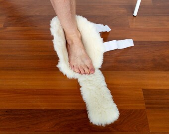 May include: A cream-colored, plush sheepskin foot wrap featuring a soft, thick fleece lining and white fabric straps with hook-and-loop fasteners designed to secure the wrap around the foot and ankle area for comfort and warmth.
