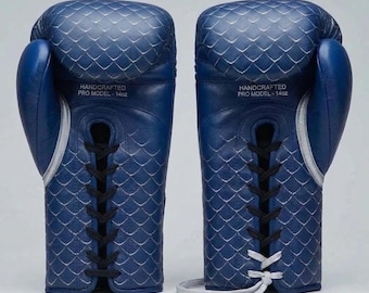 May include: A pair of blue boxing gloves with a quilted diamond pattern and black lace-up closures. The gloves feature the text HANDCRAFTED PRO MODEL - 14oz printed on the front. The right glove has black laces, while the left has white laces.