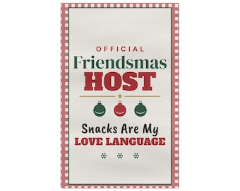 Puede incluir: Un paño de cocina rectangular blanco con un borde a cuadros rojos y blancos. El texto dice OFFICIAL Friendsmas HOST Snacks Are My LOVE LANGUAGE, acompañado de tres pequeños adornos navideños y tres copos de nieve.