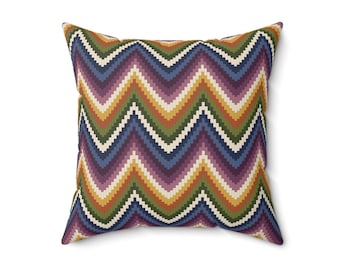 Puede incluir: Un cojín cuadrado con un patrón de chevrón repetitivo en bandas horizontales de color morado, azul, verde, amarillo y blanco. El diseño en zigzag cubre toda la superficie del cojín, creando una estética geométrica vibrante y multicolor.