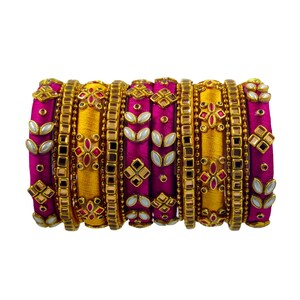 Puede incluir: Un conjunto de brazaletes que alterna bandas envueltas en seda de color magenta vibrante y amarillo dorado. Los brazaletes magenta están decorados con piedras blancas en forma de hoja y espejos cuadrados, mientras que los amarillos tienen detalles florales.