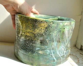 May include: A large, green, and yellow ceramic planter with a textured surface. The planter has a wide, round opening and a slightly curved body.