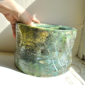 Può includere: Un grande vaso in ceramica verde e giallo con una superficie testurizzata. Il vaso ha un'ampia apertura rotonda e un corpo leggermente curvo.