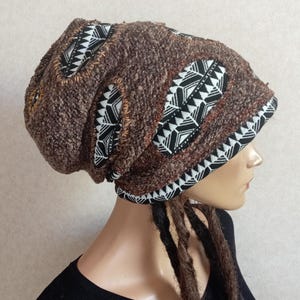 Könnte beinhalten: Eine locker sitzende Mütze aus strukturiertem, braunem Strickstoff mit eingesetzten Paneelen aus schwarz-weißem, geometrisch gemustertem Stoff. Die Mütze ist mit sichtbaren Ziernähten entlang der Kanten der kontrastierenden Stoffeinsätze versehen.