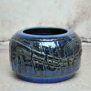 May include: A small, blue ceramic planter with a textured, crackled glaze. The planter has a wide, round opening and a slightly rounded bottom.