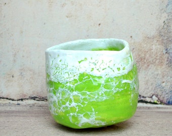 May include: A green ceramic cup with white crackle glaze. The cup has a rounded shape and a wide rim.