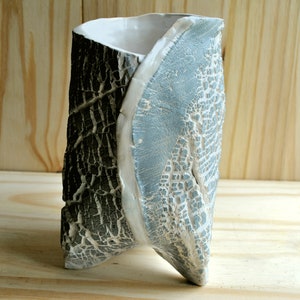 Könnte beinhalten: Eine Keramikvase mit einem einzigartigen, gedrehten Design. Die Vase ist in einem hellblauen und weißen Farbton mit einer craquelé-Oberfläche glasiert.