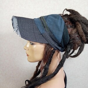 Puede incluir: Una visera confeccionada con múltiples paneles de tela en tonos gris oscuro y azul. La visera presenta una tela texturizada gris oscuro con un pequeño borde de cuadros negros y blancos. La parte superior muestra un patrón de cuadros azules.