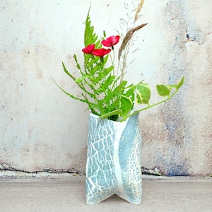 Puede incluir: Un jarrón de cerámica azul con un diseño de esmalte craquelado, que contiene un ramo de flores rojas y follaje verde.