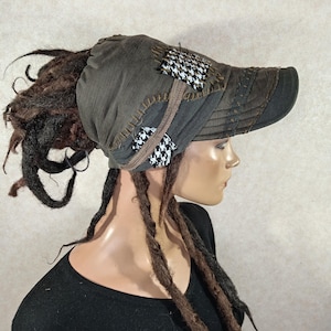 May include: A unique, olive green cap with a patchwork design. The cap features a black and white houndstooth pattern and brown stitching. The brim is dark brown. The cap is designed to accommodate dreadlocks.