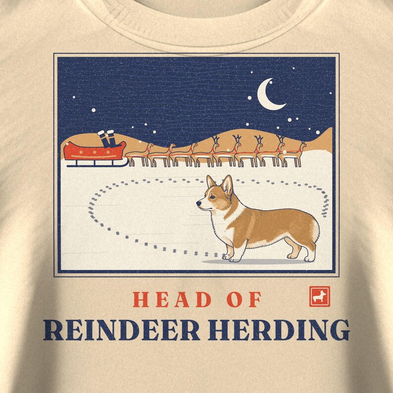 May include: A cream-colored t-shirt featuring a graphic of a Corgi standing in snow with a sleigh and reindeer in the background under a crescent moon. The text reads HEAD OF REINDEER HERDING with a small red square icon containing a white Corgi.