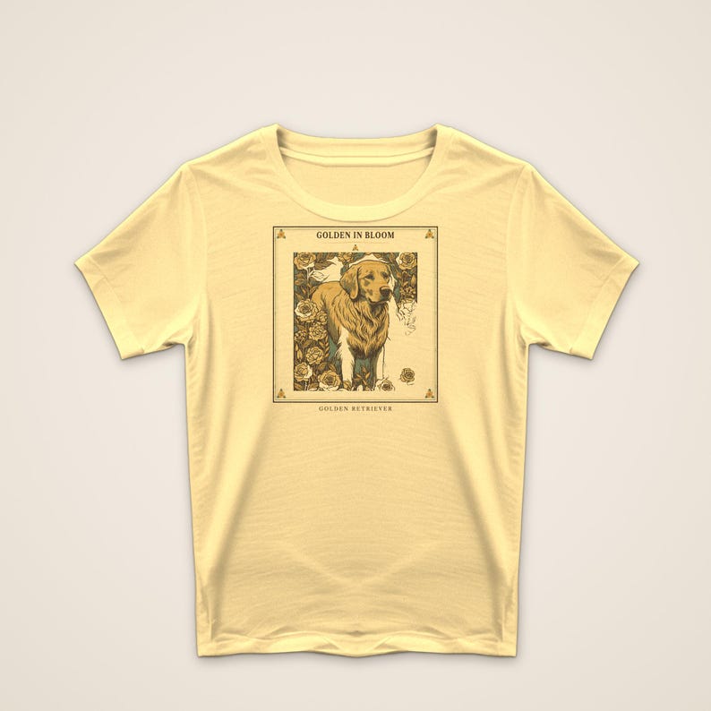 May include: A pale yellow short-sleeve t-shirt featuring a rectangular graphic print of a golden retriever surrounded by roses. The text "GOLDEN IN BLOOM" appears above the dog, and "GOLDEN RETRIEVER" is printed below the illustration.