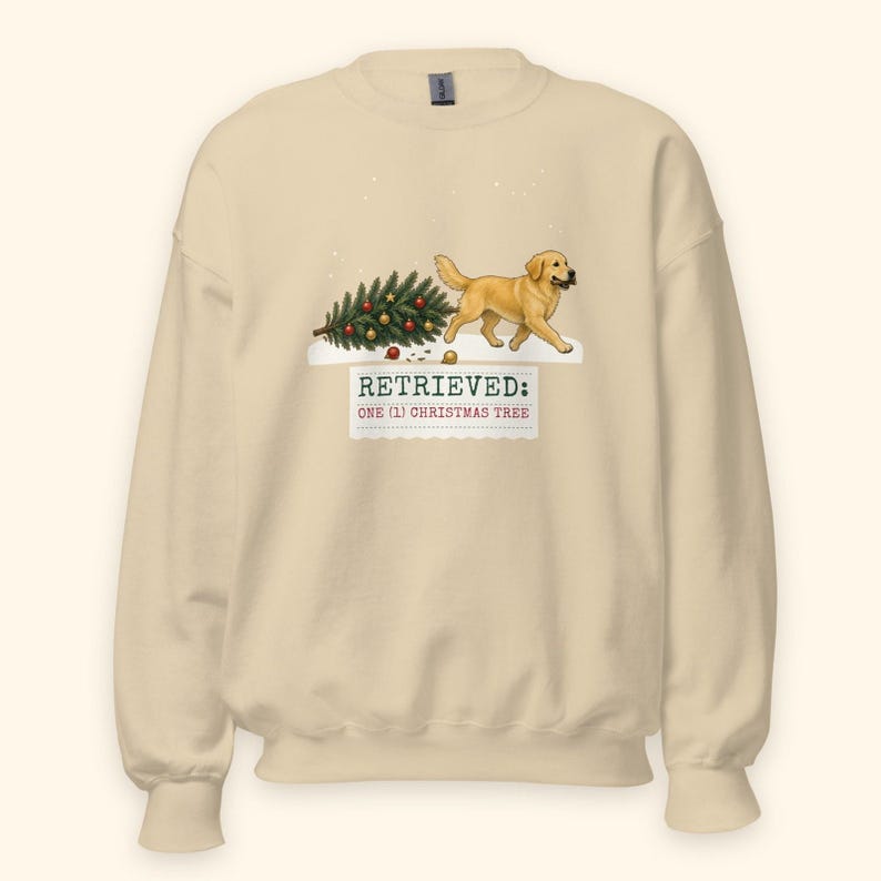 May include: A beige crewneck sweatshirt featuring a graphic of a golden retriever dog pulling a decorated Christmas tree through the snow. Below the dog, the text reads: RETRIEVED: ONE (1) CHRISTMAS TREE in dark green and red lettering.