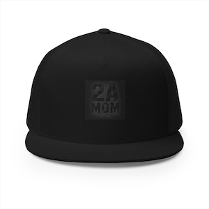 May include: A solid black trucker cap featuring a structured front panel and a mesh back. The centre of the front panel displays a square graphic with the text 2A MOM in a dark, distressed, textured font against a subtle checkered background.