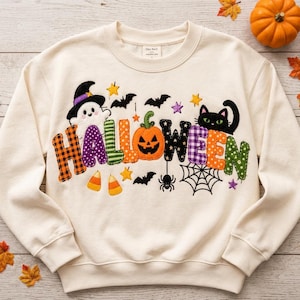 Pode incluir: Uma camisola de gola redonda cor de creme com a palavra HALLOWEEN em letras de tecido coloridas e estampadas. O design inclui um fantasma com chapéu de bruxa, uma abóbora, um gato preto, morcegos, uma aranha, uma teia e doces.