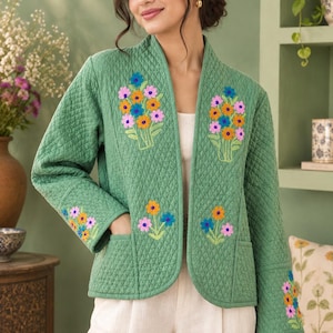 May include: A sage green quilted jacket featuring an open front, long sleeves, and two front pockets. The jacket is decorated with embroidered floral motifs in shades of blue, orange, and pink on the chest, lower front, and sleeve cuffs.