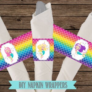 May include: DIY napkin wrappers with a rainbow mermaid scale pattern. Each wrapper features a different mermaid with a pink, blonde, or purple tail. The text "DIY Napkin Wrappers" is printed on a blue ribbon.