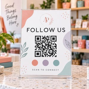 May include: A clear acrylic sign featuring the text FOLLOW US and SCAN TO CONNECT with a central QR code. The design includes a logo with the letters AP, abstract shapes in peach, lavender, and teal, and small dotted patterns on a white background.