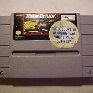 May include: A gray Super Nintendo Entertainment System (SNES) game cartridge for the game 'Race Drivin'. The cartridge has a sticker on it that says 'VIDEOSCOP III of Marblehead Village Plaza 631-7867'.