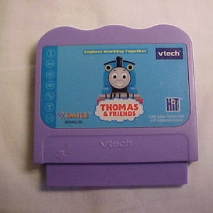 May include: Purple VTech V.Smile learning game cartridge featuring Thomas & Friends. The front of the cartridge shows Thomas the Tank Engine with the text "Engines Working Together" and "V.Smile".