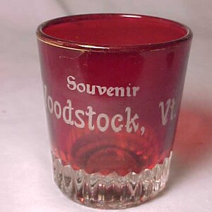 May include: A red glass souvenir shot glass with the words "Souvenir Woodstock, Vt." etched in white.