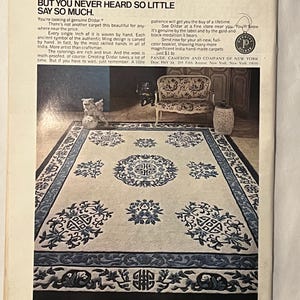 May include: An advertisement for a Dildar carpet. The carpet is cream-colored with a dark blue border and intricate floral and geometric patterns. The text reads "Money Talks. But You Never Heard So Little Say So Much."