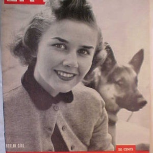 May include: A black and white magazine cover featuring a young woman with a German Shepherd dog. The magazine is titled "LIFE" and the cover story is "West Berlin, A Gay and Courageous City". The cover also includes the text "Berlin Girl" and "December 4, 1958".
