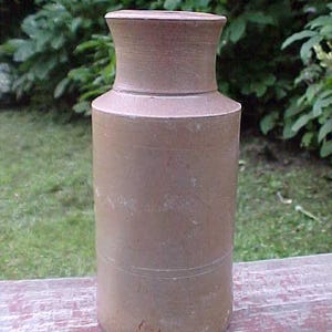 May include: A brown ceramic inkwell with a wide mouth and a rounded base. The inkwell has a smooth, slightly textured surface.