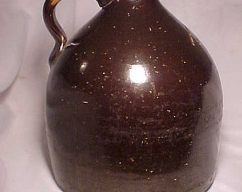 May include: A brown glazed stoneware jug with a handle. The jug has a chipped rim and a rustic appearance.