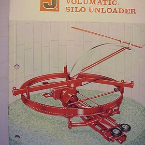May include: A red Jamesway Volumatic Silo Unloader, a piece of farm equipment used to unload grain from a silo. The machine has a large circular frame with a red metal arm extending from the top. The arm is attached to a smaller red metal frame with wheels.